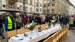 Festlich gedeckter Tisch steht auf Platz mit Menschenmenge.