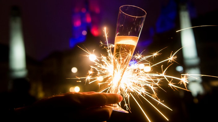 Eine Hand mit einem Glas Champagner und einer Wunderkerze.