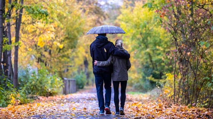 Goldener Oktober mit Spaziergängern, junges Paar mit Regenschirm