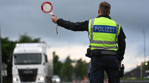 Ein Polizist mit gelber Warnweste hält auf einer Straße einen LKW an