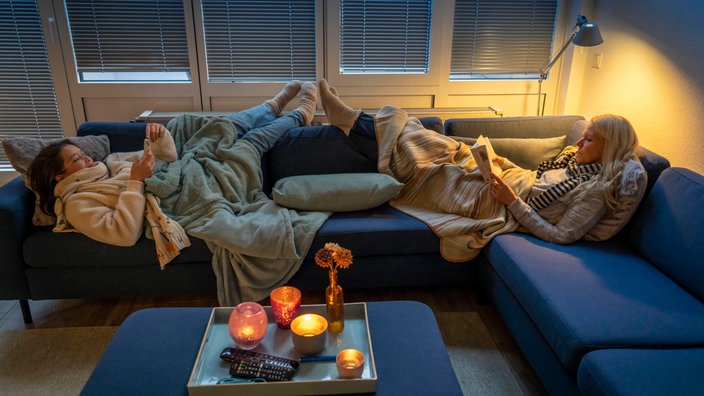 Mutter und Tochter liegen warm angezogen auf dem Sofa