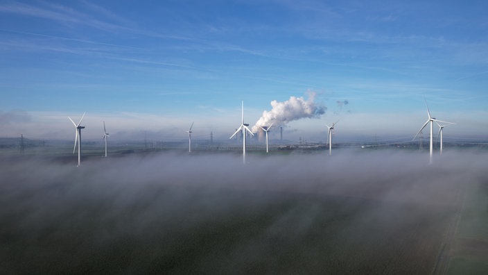 Nebelschwaden ziehen über das Land. Aus dem Nebel heraus ragen Windräder.