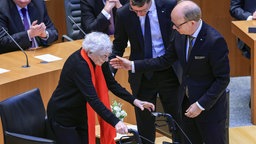 Hendrik Wüst, Ministerpräsident von Nordrhein-Westfalen, Andre Super , Landtagspräsident, helfen Ruth Weiss, Journalistin und Schriftstellerin, während einer Gedenkstunde für die Opfer des Nationalsozialismus im Landtag auf dem Weg zum Rednerpult.