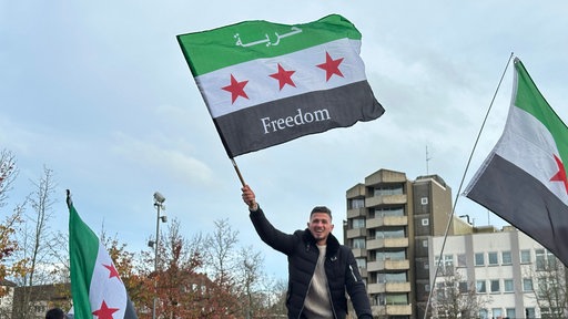 Ein Mann steht und schwenkt eine syrische Flagge mit der Aufschrift Freiheit