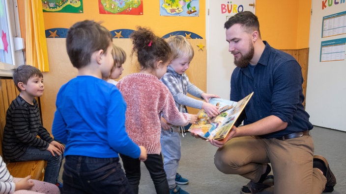 Ein Erzieher liest Kindern aus einem Buch vor