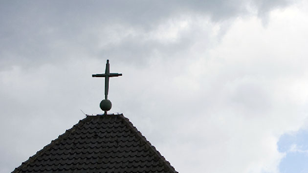 Wolkenverhangener Himmel zeigt sich über einem Kreuz einer katholischen Kirche.