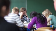 Lehrerin sitzt erschöpft mit Schülern am Tisch