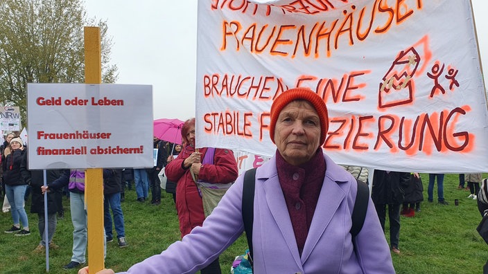 Marion Steffens hält ein kleines Plakat mit der Aufschrift " Geld oder Leben. Frauenhäuser finanziell absichern!"