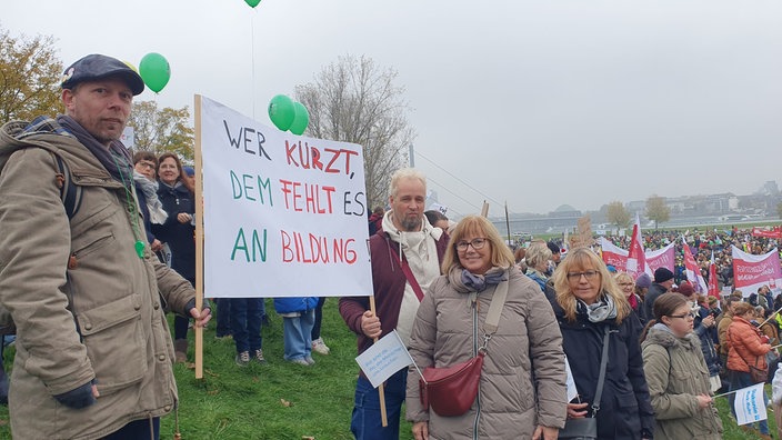 Zwei Männer halten ein Plakat mit der Aufschrift "Wer kürzt, dem fehlt es an Bildung", neben ihnen steht Annette Jeschak und lächelt freundlich.