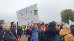 Eine Frau hält ein Plakat hoch, auf ihm steht: "Refugees welcome! Geflüchtete brauchen Beratung!"