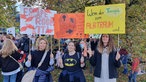 Drei Erzieherinnen halten ihre selbstgemalten Plakate hoch bei einer Demonstration vor dem Landtag in Düsseldorf.