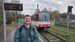 Student steht an einer Straßenbahnstation