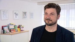 Andreas Pamp steht in seinem Büro und lächelt.