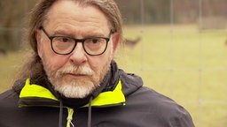 Jagdwissenschaftler und Wildtierökologe Dr. Jörg Brün trägt schwarze Brille und einen braunen Pferdeschwanz. Sein Vollbart ist grau.