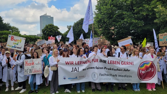 Viele junge Menschen in weißen Arztkitteln stehen zusammen mit Bannern, Transparenten und Plakaten