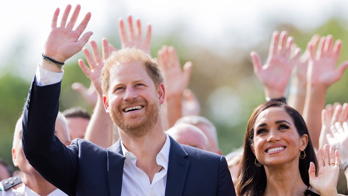 Prinz Harry, Herzog von Sussex, und seine Frau Meghan, Herzogin von Sussex, am Rande der Invictus Games in Düsseldorf, beide winken freundlich lächelnd.