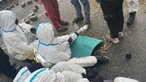 Aktivisten in weißen Anzügen mit blauen Streifen sitzen in Lützerath auf einer Straße, auf der Pflastersteine liegen.