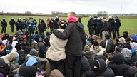 Ein Mann hält Frau im Arm, vor ihnen eine Sitzblockade. Dahinter Polizisten