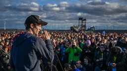 Henning May von der Band AnnenMayKantereit stehen in Lützerath auf einer Bühne am Rand des Tagebaus.