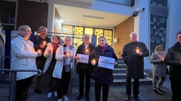 Einige Menschen halten Kerzen und Schilder und stehen vor der Synagoge.