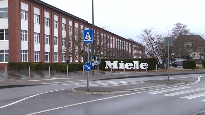 Außenansicht des Miele-Werks mit einem Schild mit dem Miele Schriftzug davor