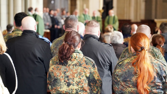 Soldatinnen und Soldaten stehen in den Kirchenbänken und feiern einen Gottesdienst