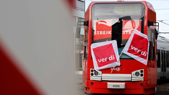 Eine KVB-Bahn mit Ver.Di Flaggen geschmückt steckt auf den Gleisen. In ihren Fenstern hängen zwei Poster mit der Aufschrift "Streik"