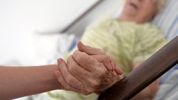 Eine Krankenschwester hält die Hand einer Bewohnerin eines Pflegeheims