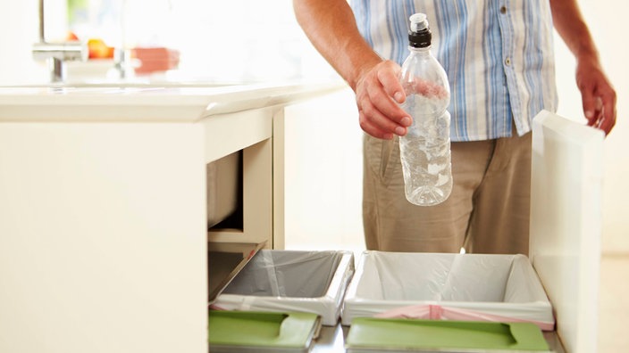 Eine Person wirft eine Plastikflasche in einen Hausmülleimer in einer Küche