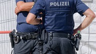 Zwei Polizisten stehen sich gegenüber, an ihren Hüften tragen sie ihre Dienstwaffe