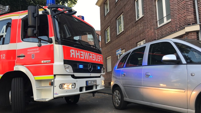 Ein Feuerwehrwagen und ein Auto stehen in einer engen Straße