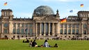 Menschen sitzen auf der Wiese vor dem Reichstagsgebäude in Berlin