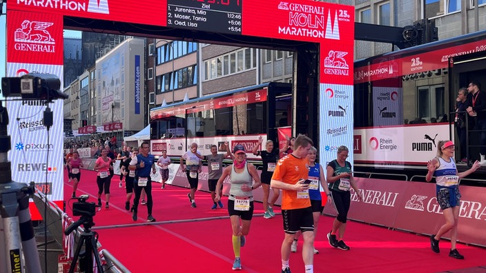 Menschen laufen über das Ziel beim Köln Marathon 2023. Sie jubeln und sind begeistert.