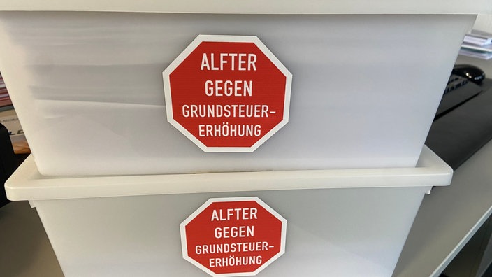 Zwei weiße Kunststoffkisten aufeinander gestapelt, mit der Aufschrift "Alfter gegen Grundsteuererhöhung"