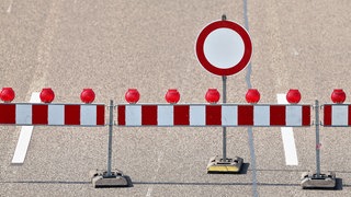 Auf dem Foto ist eine Autobahn mit mehreren Fahrbahnen, vor der mit einem Zaun und einem Schild eine Sparrung markiert ist.