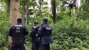 Drei Polizisten mit Helmen stehen im Wald, dahinter Plakate in den Bäumen.