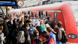 Zu sehen ist ein voller Bahnsteig mit einer Vielzahl von Menschen, die alle versuchen einen Zug zu betreten der im Gleis hält.