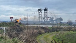 Ein kleines Feuer am Rande des Tagebaus, im Hintergrund ein Braunkohlebagger