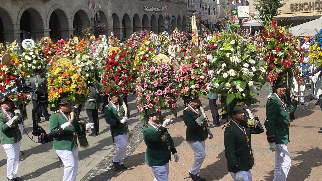 Parade mit Männern in Schützentracht und Blumenkränzen 