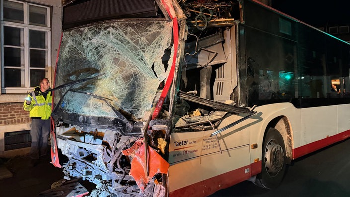 Linienbus mit zerstörter Front nach Kollision mit einer Hauswand.  