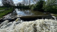 Ein Fluss fliesst an einem Deich entlang dann die Stromschnelle voll im Bild unten