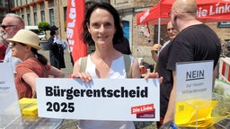 Frau mit großem Schild, nebendran eine Abstimmungsurne