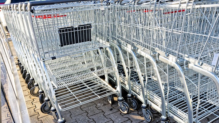 Auf dem Foto sind mehrere Einkaufswagen, die ineinandergeschoben in ihrem Depot vor einem Supermarkt stehen.