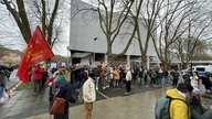 Vor dem Universtitätsgebäude stehen Demonstrierende mit palästinensichen Flaggen