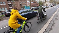 Zwei Radfahrer auf einer Straße in Mönchengladbach, gerade werden sie von einem Auto überholt.