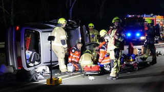 Einsatzkräfte neben einem verunfallten Auto.