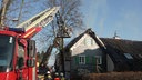 Das brennende Fachwerkhaus im Hintergrund, davor ein Feuerwehrauto mit Drehleiter und Korb, in dem löschende Feuerwehrleute stehen