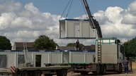 Mehrere Container stehen nebeneinander, eins wird gerade mit einem Kran verladen