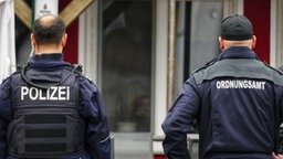 Beamte der Polizei und des Ordnungsamts in Uniform von hinten vor einem Gebäude, das kontrolliert wird