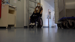 Eine Frau im Rollstuhl die durch einen Flur geschoben wird. 